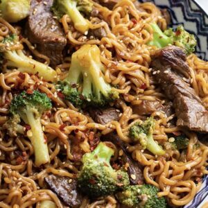 A plate of noodles with meat and broccoli.