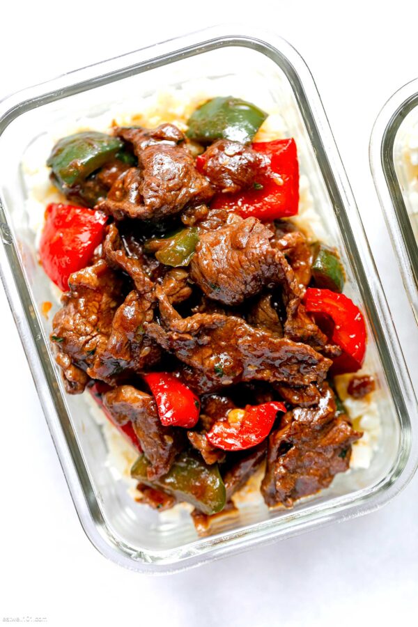 A glass container with meat and peppers in sauce.