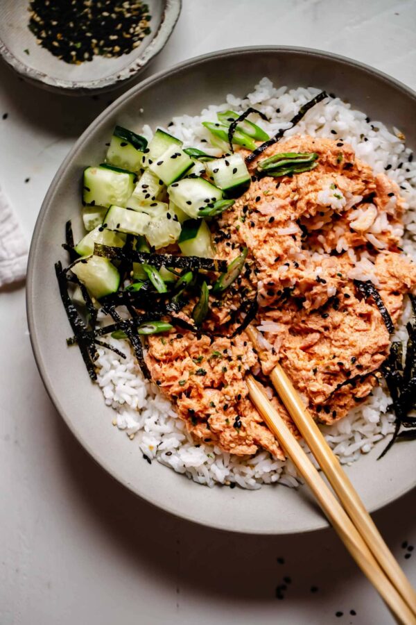 A bowl of rice and vegetables with chopsticks.