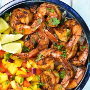 A bowl of shrimp and fruit with lime wedges.