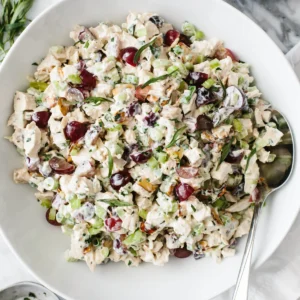 A bowl of salad with grapes and nuts.