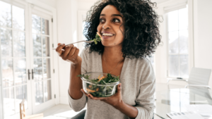 A woman holding a bowl of salad and eating it.